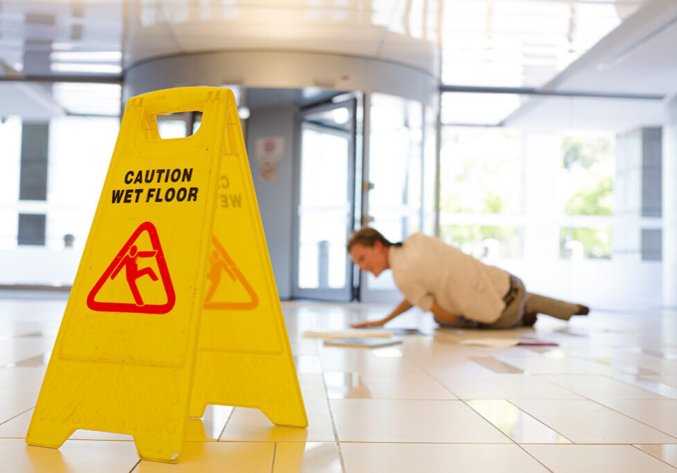 Wet floor sign standing in the foreground with a man on the ground behind it