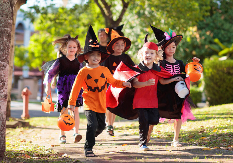 Children in Halloween costumes skipping down a sidewalk