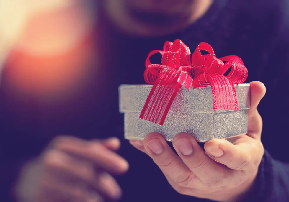 Man holding out a small box with a red bow on top