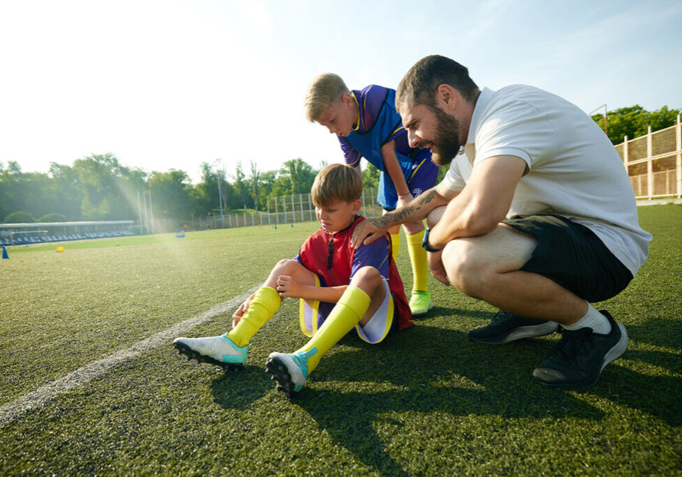 coach and teammate check in on a young player with an injury to his leg